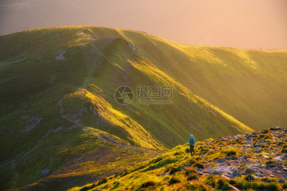 美丽的山雾中和站着女士带背包在山峰上夏天日落的山峰上风景与女孩一起在小路上石头绿山阳光照亮的青山旅行和游图片