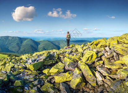 美丽的山峰和站立年轻女子夏天日落时背着包在绿石上山顶森林丘蓝天空和云层上有运动女孩的风景图片