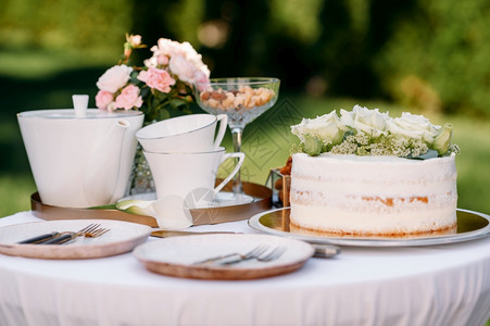 餐桌设置陶瓷茶壶杯蛋糕和鲜花特写侧面看没有人白桌布上的豪华银器户外餐具桌设置茶壶蛋糕图片