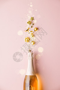 彩带星圣诞球和彩蛋的金装饰品从香槟酒瓶中飞来平躺节日概念欢庆香槟酒瓶和粉红背景的金装饰品图片