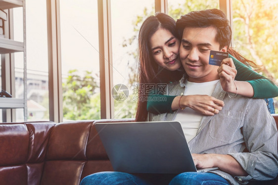 年轻夫妇在家中的互联网站上使用信卡在线购物信用卡号码是假冒的信用卡上没有个人信息网上商业购物概念图片