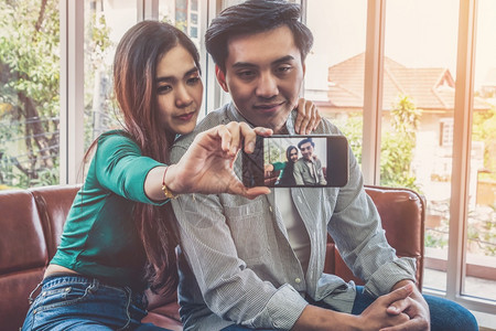 快乐的亚洲情侣在客厅用手机自拍图片