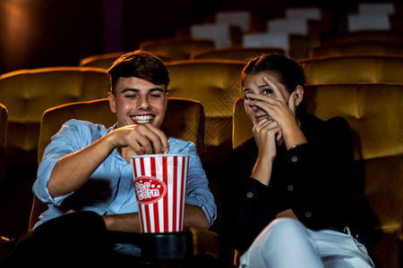 一对夫妇的caucasiansian在电影院看一部惊魂片女人的眼睛闭着把她的脸从屏幕上转开图片