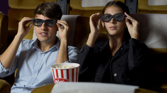 电影中的男人和女观看一部三维眼镜的电影有兴趣观看屏幕奋和吃爆米花图片