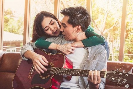 亚洲小情侣一起在家中的客厅玩吉他和唱歌音乐生活方式概念图片