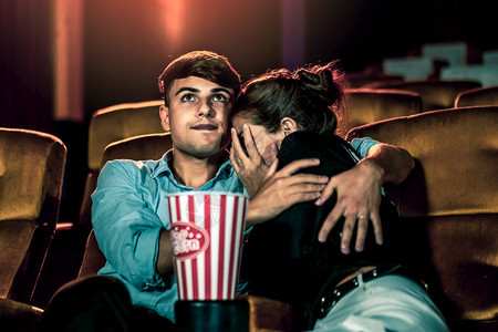 一对夫妇的caucasiansian在电影院看一部惊魂片女人的眼睛闭着把她的脸从屏幕上转开图片