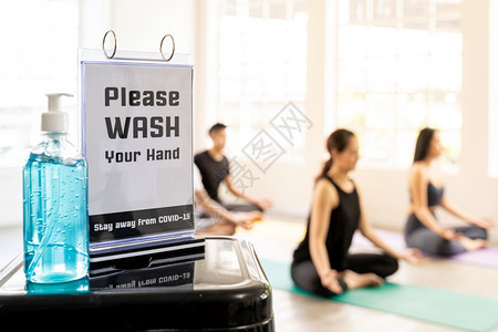 在具有瑜伽班学生和教练背景的新正常健身房里用手洗牌来酒精凝胶或洗手液净化剂以防止新冠19冠状流行图片