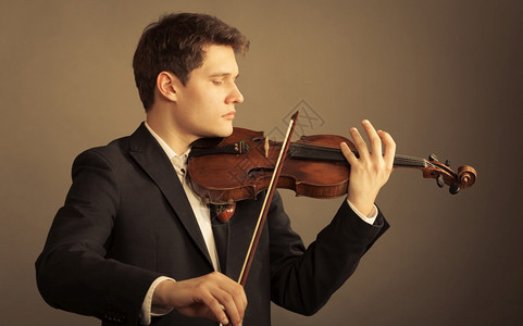 年轻优雅的小提琴家手在棕色和古典音乐上拉小提琴图片
