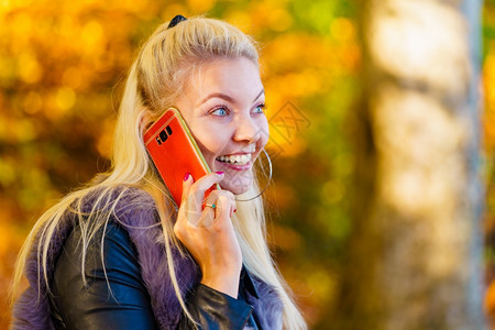 穿着时装的金发美女在秋季公园散步用智能电话交谈图片