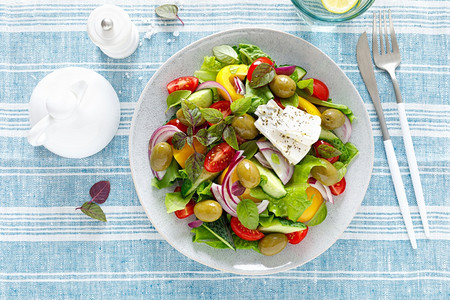 希腊沙拉新鲜蔬菜包括黄瓜西红柿橄榄洋葱胡椒白菜奶酪生和草药并配有盐胡椒和橄榄油图片