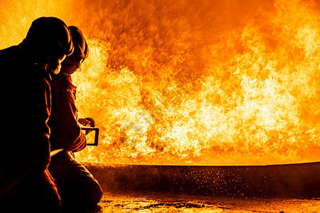 消防员使用Twirl水雾型灭火器与油的焰抗争以控制火势不扩散消防员和工业安全概念图片