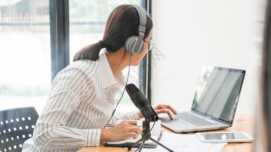 亚洲女播客在工作室和录制在线脱口秀使用耳机专业麦克风和电脑笔记本在桌面上观看无线电播客的相机图片