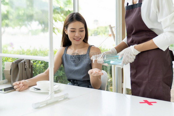 服务员在餐桌为上的顾客提供酒精凝胶洗手剂用于清洁卫生减少感染传播新冠新冠19大流行图片