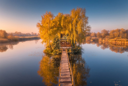 秋天日出时旧渔夫老屋和木码头空中观景湖边小岛上有房子的美丽风景多彩树木码头水面反射在乌克兰坠落顶端观景背景图片