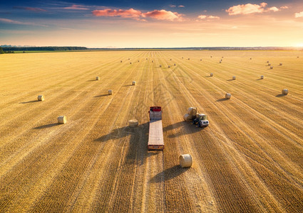 农业机械日落收割粮食作物之后的查封田地和干草堆顶层视图拖拉机在卡车上装载大量干草拖车背景图片