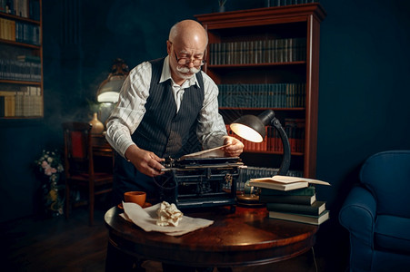 老年人作家将纸张插入其办公室的老式打字机年人在房间里写文学小说在桌上放烟雾灵感咖啡和折叠床单老年人作家将纸张插入打字机图片