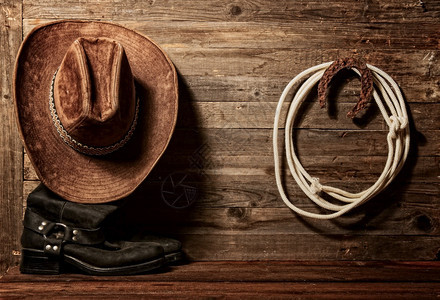 非常生锈的老马蹄木象征着好运和拉索挂在木墙上牛仔帽和靴子上图片