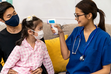 亚洲女医生使用红外温度计对小女孩与父亲一起坐在居室而医生则到家里看病图片