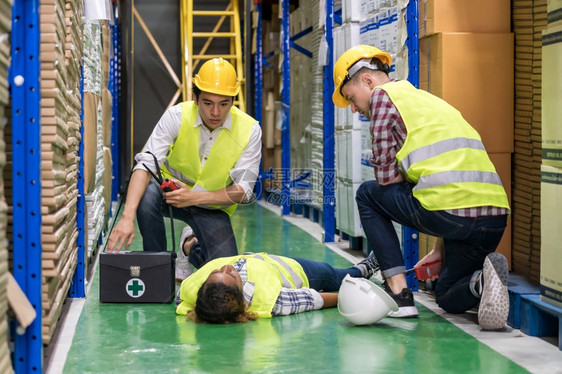 仓库工人在作时对伤事故后躺仓库地板上的同事进行急救使用工业安全第一概念和企业保险图片
