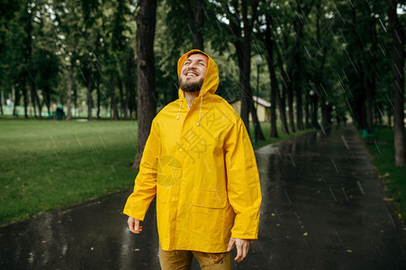 穿着雨衣的男子享受夏季公园的雨穿着披风的男子在步行路上快乐巷子里的湿天气穿雨衣的男子享受夏季公园的雨图片