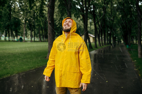 穿着雨衣的男子享受夏季公园的雨穿着披风的男子在步行路上快乐巷子里的湿天气穿雨衣的男子享受夏季公园的雨图片