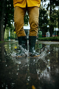 男子在雨蓬和橡皮靴中跳到水坑在巷子里的湿天气中跳到水坑男子在夏季公园雨水保护滴中男子在橡胶靴中跳到水坑男子在池保护滴中男子在橡胶图片