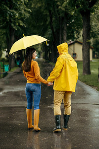 雨天在夏季公园散步的情侣和有雨伞男人和女穿着橡胶靴在路上行走巷子里的湿天气带雨伞的情夫妇在季行走图片