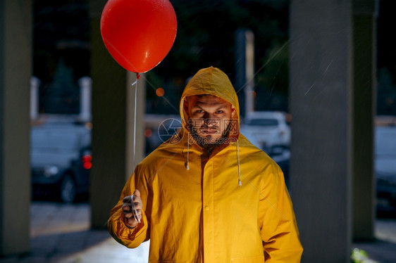 雨天夏夜公园里走着气球的可怕男子陌生穿着雨披风在巷子里的湿天气在夜公园里走着气球的可怕男子图片