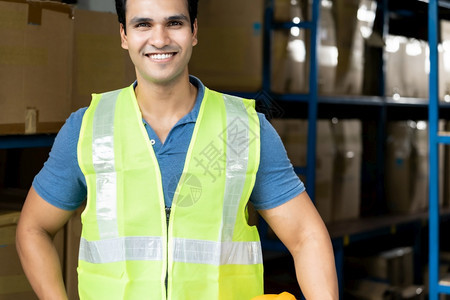 印度亚洲仓库工人的肖像有安全背心站在仓库分发中心环境持有黄色头盔图片