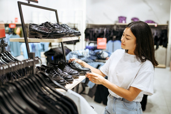 女青年在服装店中选择鞋子女青年在时装店商购物偷看靴子的购物女青年在服装店中选择鞋子图片