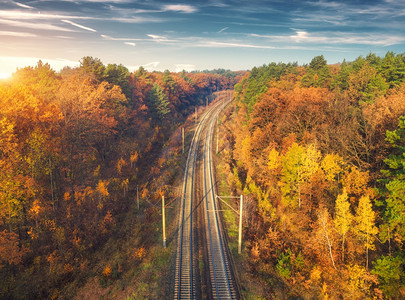 日落时秋天森林中美丽的铁路空中景色工业观与火车站蓝色天空与云彩树木色橙叶子秋季农村铁路的顶端景色背景图片