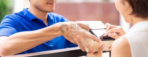 全亚洲女在接受穿蓝衬衫男生员的包后在便携式移动设备上签名包件购物和数字标志概念图片