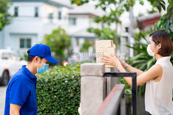 身戴面罩的侧女客户从送货员为无接触分娩而安装的围栏站上购买物包这可以减少新冠新冠19的传播图片