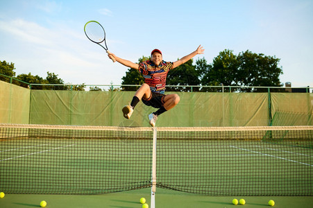 快乐的男网球运动员在户外法庭上与网球赛一起在中跳跃积极的健康生活方式体育比赛健身训练与斗篷快乐的男网球运动员与一起跳跃图片