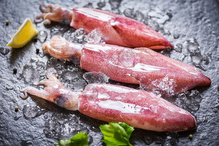 冰上的生鱿鱼和黑盘海鲜市场柠檬新鱿鱼章或熟食沙拉餐厅的鱼图片