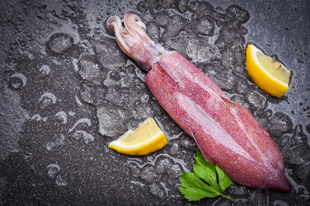 新鲜鱿鱼章或熟食沙拉餐厅在冰上生鱿鱼黑盘海鲜市场加柠檬图片