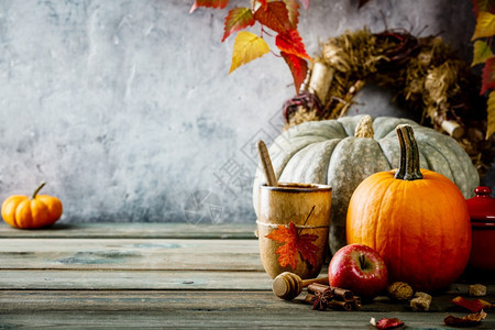 秋幕背景茶杯或咖啡南瓜派香料和木制餐桌边的叶子与古老生锈状况墙壁文字空间相对照图片