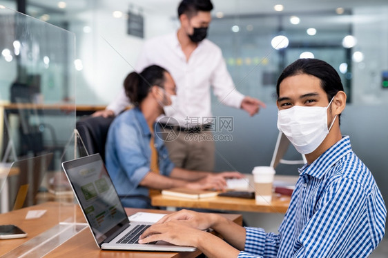 亚洲办事处有防护面罩的雇员在新正规办公室工作与背景同事在社会距离做法下工作防止科罗纳新冠19的传播图片