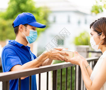 亚洲人用蓝色衬衫搬运包送男人并给家里的年轻女服装师她们戴面罩以减少新冠新冠19的传播套件购物交付概念图片