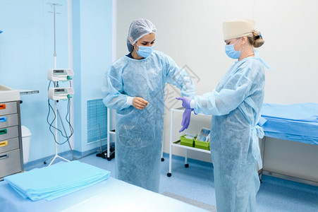 女外科医生和助理在手术室戴上套准备外科术穿制服的医生疗诊所工作人员医药和保健院的图片