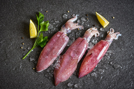 冰上的生鱿鱼和黑盘海鲜市场柠檬新鱿鱼章或熟食沙拉餐厅的鱼图片