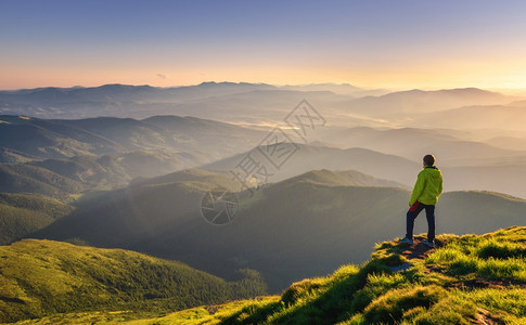 山峰上的运动男子在山峰上仰望着谷在欧洲秋天的多彩日落时带着阳光照耀太山峰游人迷雾的山坡森林倒塌惊人的天空和阳光倒塌的风景山峰上运背景图片