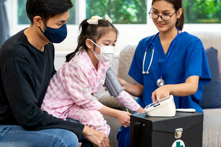 亚洲女医生测量了小童的血压让她们与父亲一起坐在居室医生回家看病庭保健分娩和医生看病概念图片