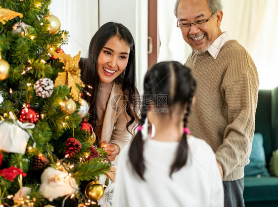 多代亚洲家庭装饰圣诞树母亲女儿和祖父装饰圣诞树为快乐和节日的季问候做准备图片