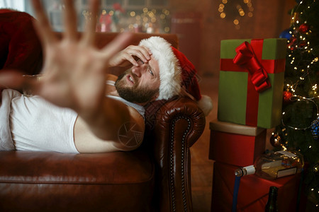 糟糕的圣誕老人有宿醉睡在沙发上恶心的派对幽默感不健康的生活方式在节日服装新年和酗酒中留胡子的男坏圣誕老人有宿醉症睡在沙发上图片