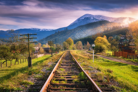 山上铁路秋天日落时有雪峰工业地貌包括火车站橙树绿草建筑物岩石紫色天空和秋的云层图片