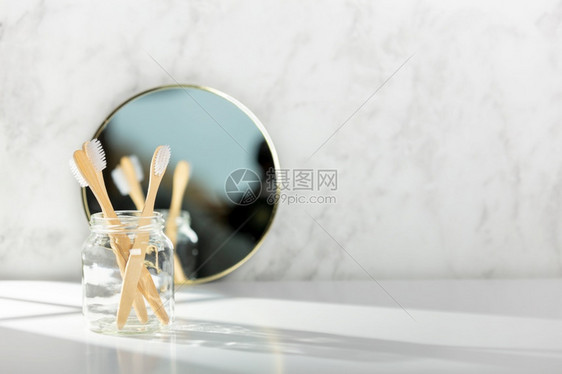 在浴室白色大理石墙附近的玻璃中竹牙刷和镜子图片