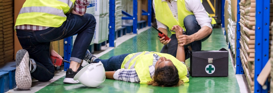全景仓库工人在作时对同事伤故后躺仓库地板上进行急救使用工业安全第一概念和企业保险图片
