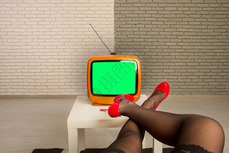 女孩坐在一个小旧电视机前绿屏在电视幕上将双腿扔在桌子上图片