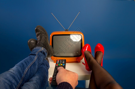 一对已婚夫妇在小台旧电视前双脚坐在桌子上并用遥控器打开了它图片